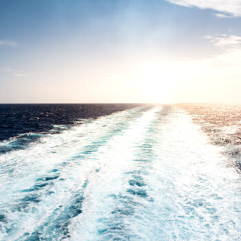 Foamy trail of sailing cruise ship on the Mediterranean Sea on a summer vacation day. No people. Peaceful seascape with small waves, calm sea and sun.